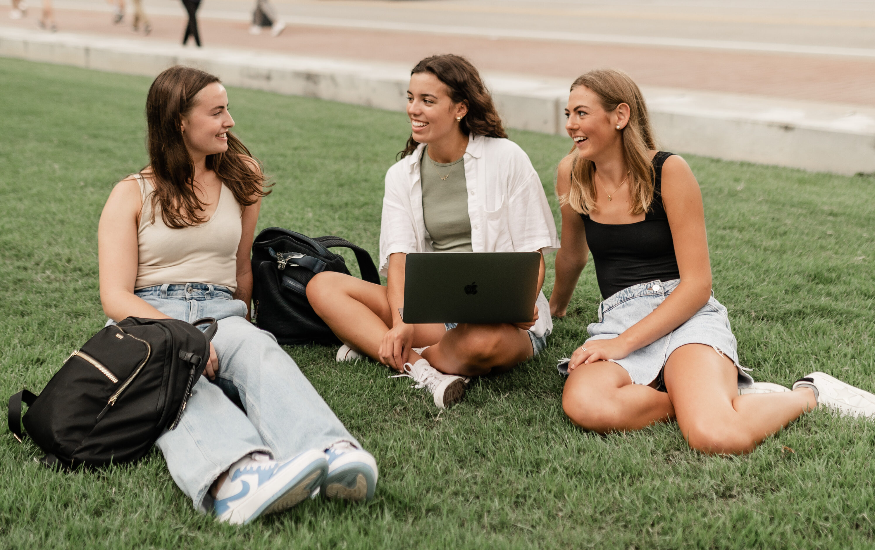 three girls sitting in the park working on a computer together