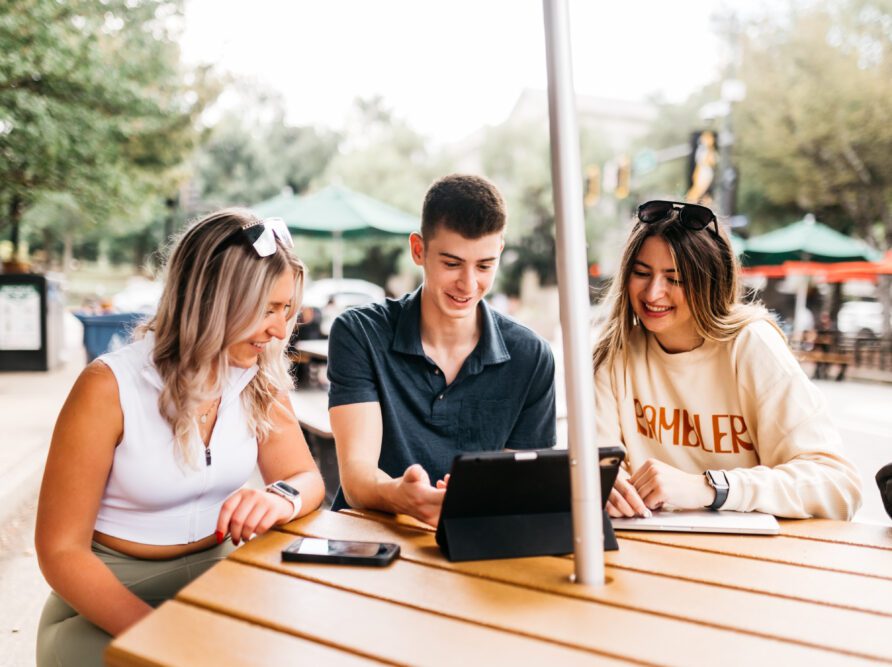 three friends sitting at a table working on a computer together