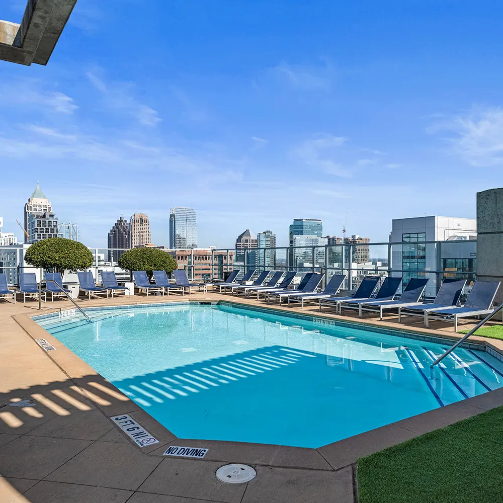 Rooftop swimming pool with lounge chairs and potted trees, overlooking a city skyline with modern and historic buildings under a clear blue sky—perfect for your next Standard Atlanta review.